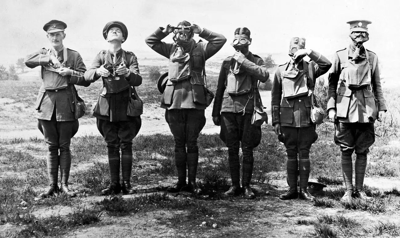 黑白照片：六名一战士兵站成一排，从左到右一步步戴上小盒式呼吸器，最后一人已完全戴好