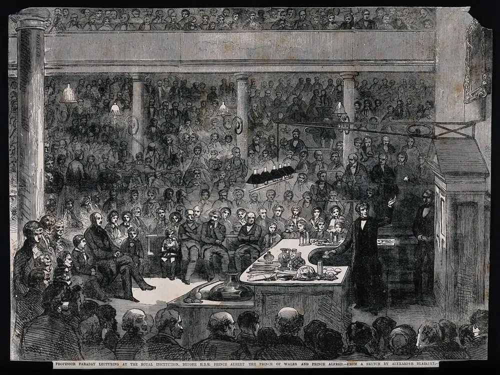 1856 年的木刻：法拉第站在讲台后演讲，阶梯座位上坐满听众，前排是阿尔伯特亲王与两位王子